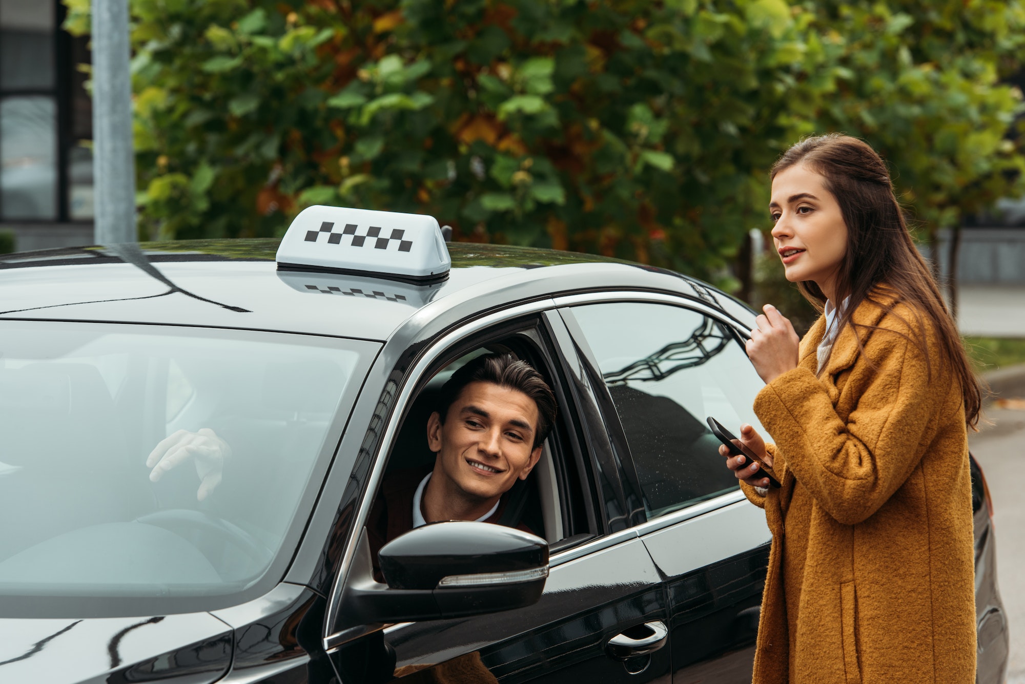 young woman holding smartphone and talking to smiling taxi driver.jpg